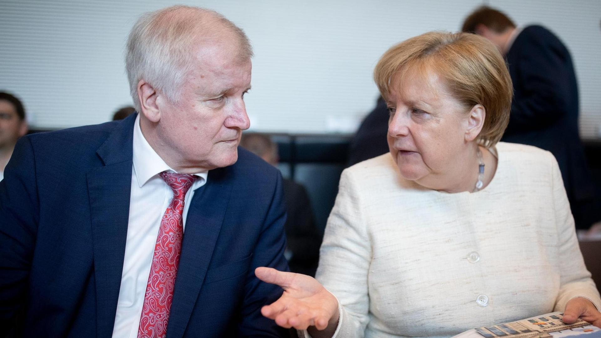 12.06.2018, Berlin: Bundeskanzlerin Angela Merkel (CDU) und Horst Seehofer (CSU), Bundesminister für Inneres, Heimat und Bau unterhalten sich Beginn der CDU/CSU-Fraktionssitzung im Bundestag.