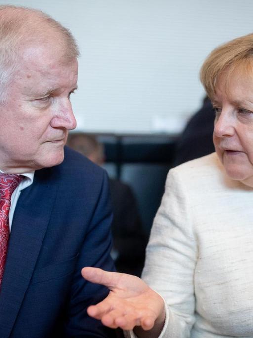 12.06.2018, Berlin: Bundeskanzlerin Angela Merkel (CDU) und Horst Seehofer (CSU), Bundesminister für Inneres, Heimat und Bau unterhalten sich Beginn der CDU/CSU-Fraktionssitzung im Bundestag.