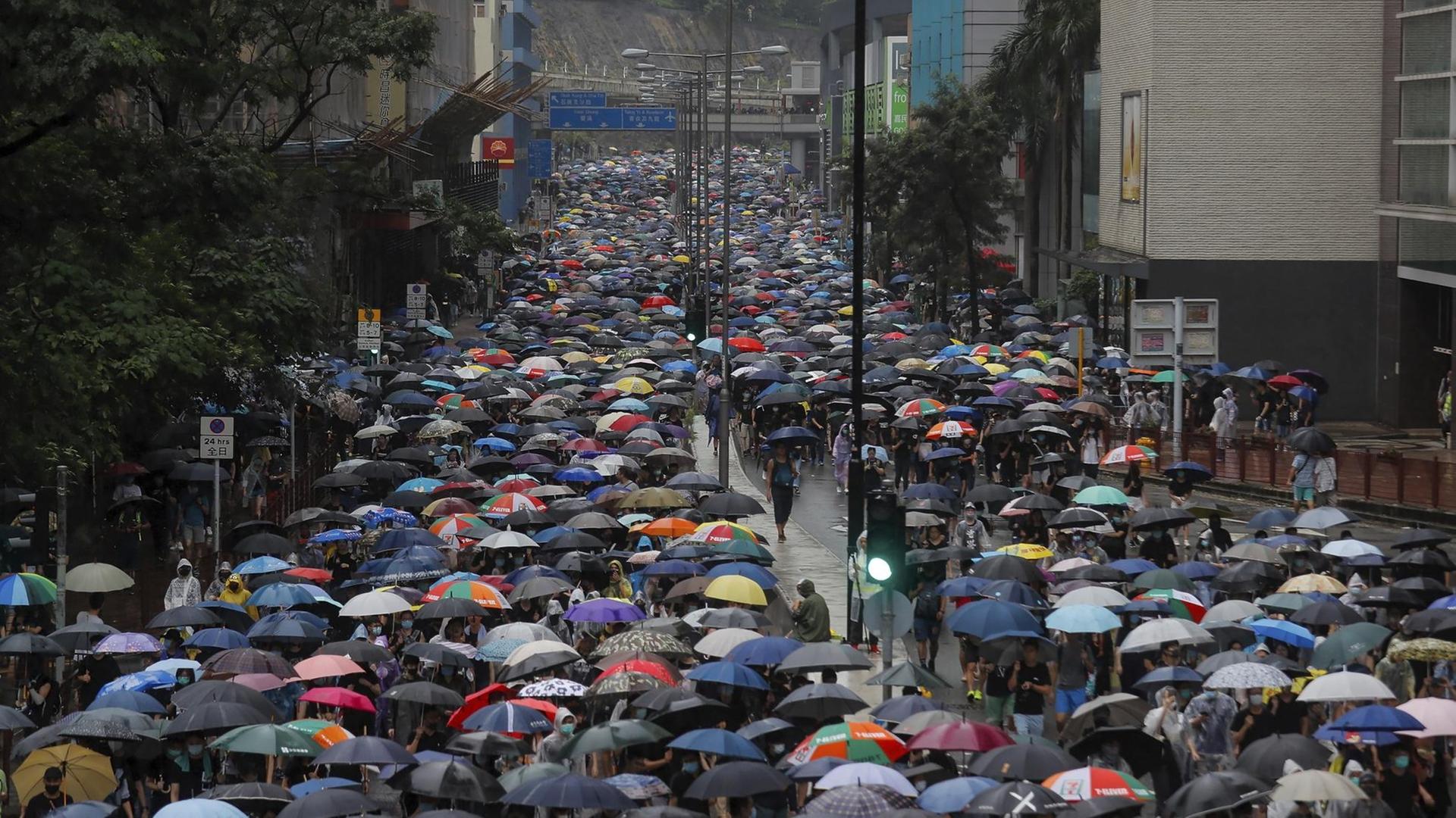 Ein langer Demonstrationszug mit tausenden Regenschirmen zieht eine breite Straße entlang durch eine Häuserschlucht. Ein langer Demonstrationszug mit tausenden Regenschirmen zieht eine breite Straße entlang durch eine Häuserschlucht.