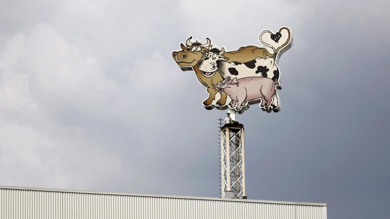 Logo der Lebensmittelfirma Tönnies bestehend aus einem Bullen, einer Kuh und einem Schwein am Hauptsitz in Rheda-Wiedenbrück vor dunklen Wolken.