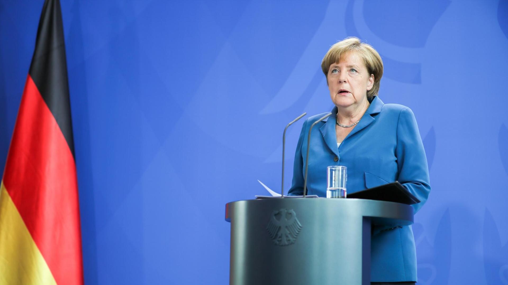 Sie sehen Bundeskanzlerin Merkel an einem Stehpult, links eine Deutschlandfahne.