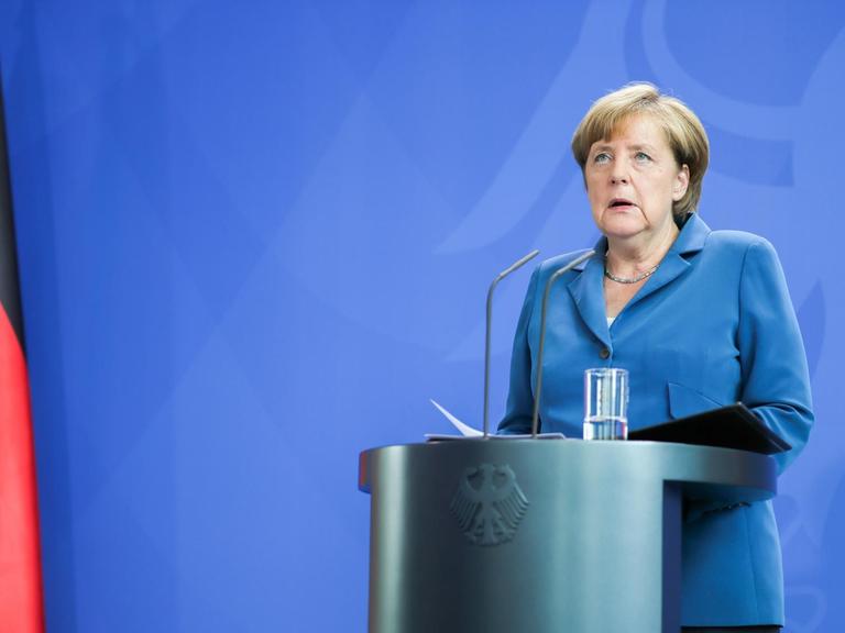 Sie sehen Bundeskanzlerin Merkel an einem Stehpult, links eine Deutschlandfahne.