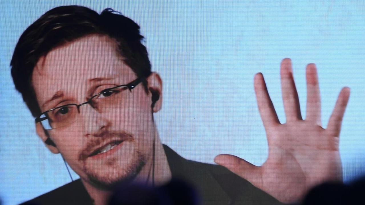 Über verschatteten Sitzreihen scheint ein auf die Bühne projizierter Stream auf, über den Edward Snowden an einer Konferenz teilnimmt. Über verschatteten Sitzreihen scheint ein auf die Bühne projizierter Stream auf, über den Edward Snowden an einer Konferenz teilnimmt.