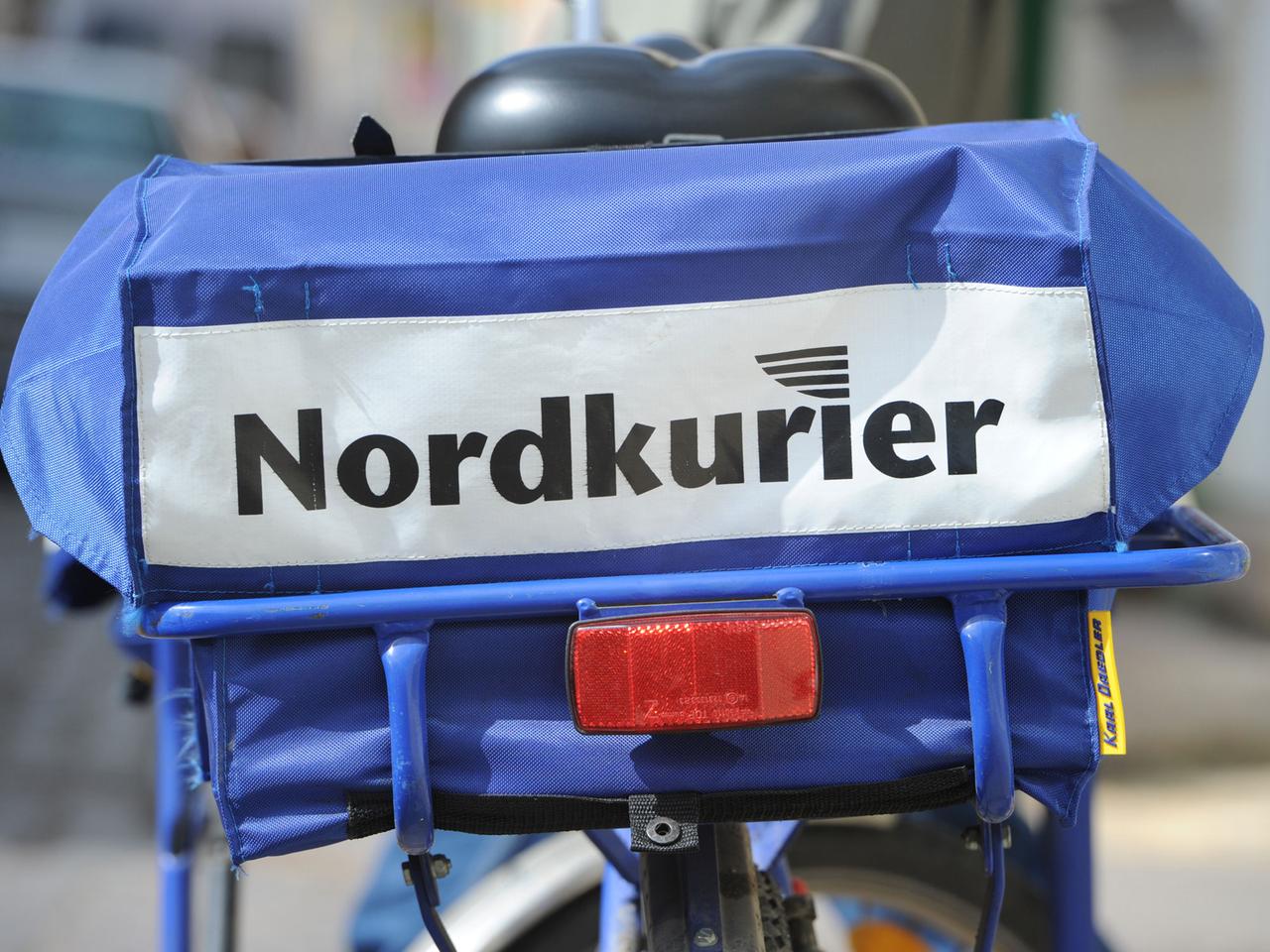 Ein Zusteller (Briefträger) vom Nordkurier Briefdienst und Paketservice hat in Stralsund sein Rad auf der Straße abgestellt, an dem das Logo der Firma zu sehen ist.