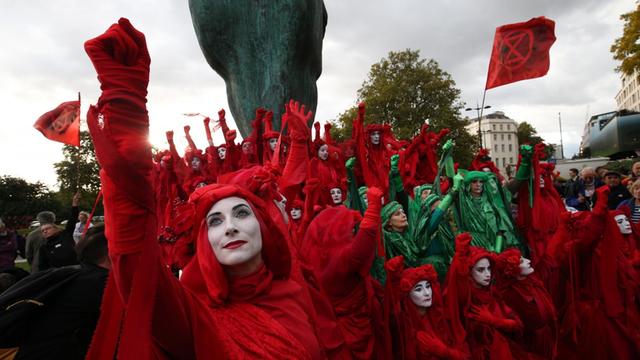 Das Foto zeigt rot und grün verkleidete Mitglieder der Gruppe Extinction Rebellion bei einer Protestaktion in London.