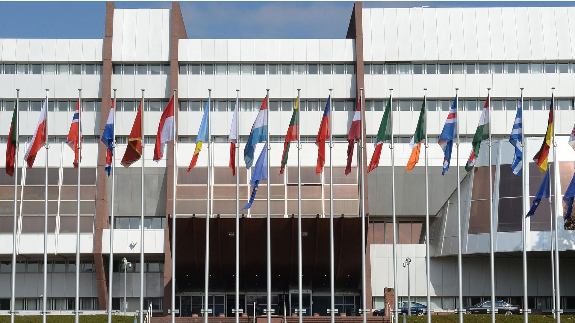 Zu sehen ist das Gebäude des Europarats in Straßburg und davor eine Vielzahl europäischer Flaggen.