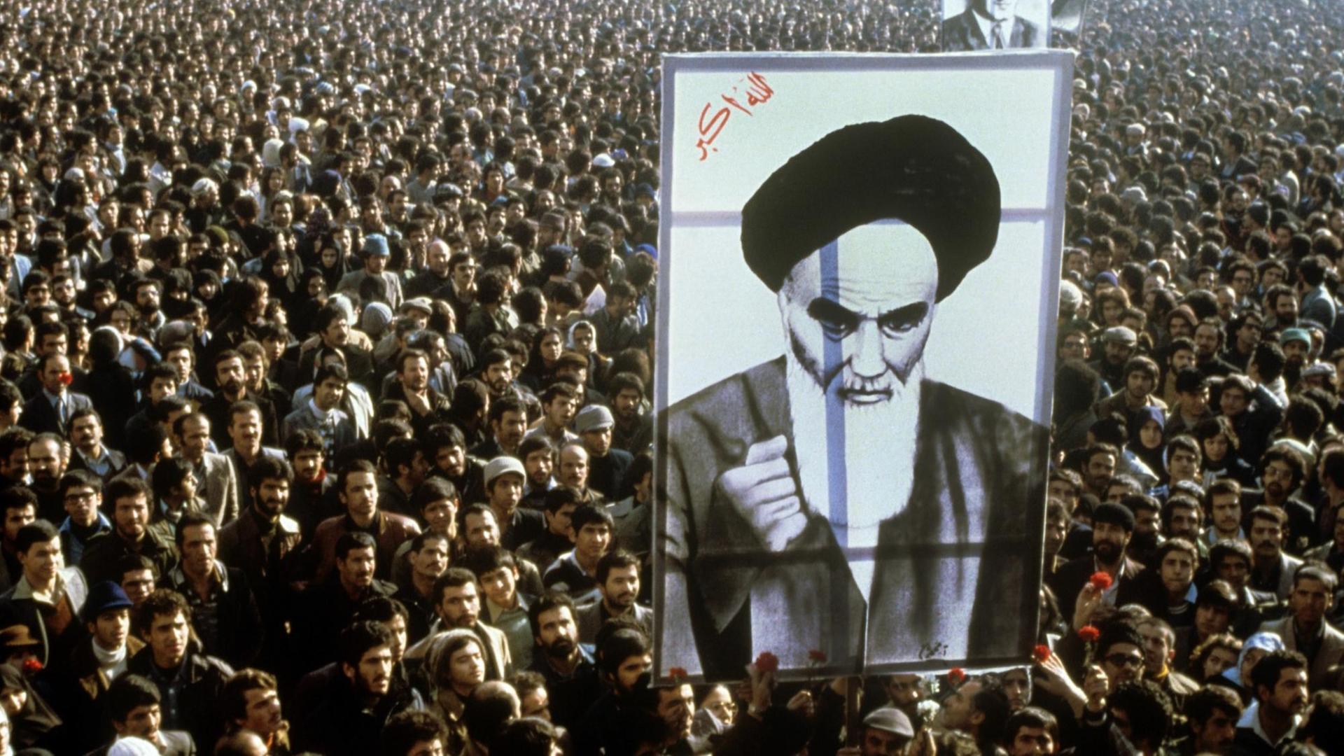 Iranische Bürger protestieren im Jahr 1979 gegen den Schah. Im Vordergrund ist ein riesiges Banner mit dem Abbild von Revolutionsführer Ruhollah Khomeini