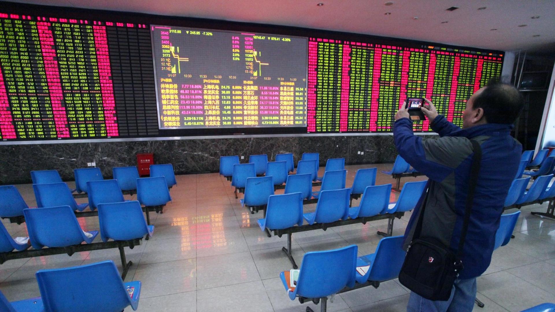 Ein chinesischer Investor fotografiert eine Anzeigetafel für Aktienkurse, nachdem der Handel kurz nach Öffnung der Börse am 7.1.2016 gestoppt wurde. Grüne Zahlen zeigen fallende Kurse.