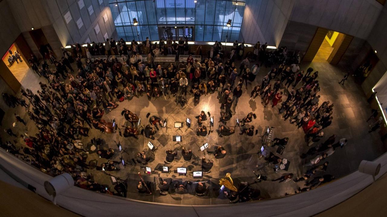 Eröffnung der Ausstellung "Peace Is Power" von Yoko Ono im Museum der bildenden Künste Leipzig. Die Kamera blickt von oben auf das Publikum und ein Orchester während der Eröffnungsveranstaltung, 2019.