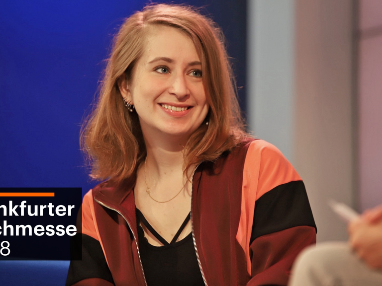 Die Autorin Margarete Stokowski lächelt die Moderatorin auf dem Blauen Sofa auf der Frankfurter Buchmesse 2018 an.