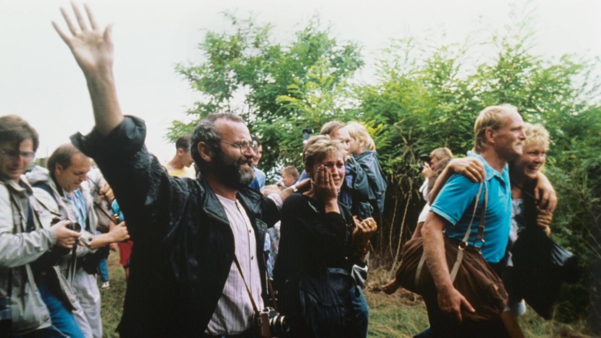 Das Foto zeigt jubelnde DDR-Flüchtlinge, die am 19.8.1989 die Grenze zu Österreich erreichen und eine symbolische Grenzöffnung für die Flucht in den Westen nutzen. Das Foto zeigt jubelnde DDR-Flüchtlinge, die am 19.8.1989 die Grenze zu Österreich erreichen und eine symbolische Grenzöffnung für die Flucht in den Westen nutzen.