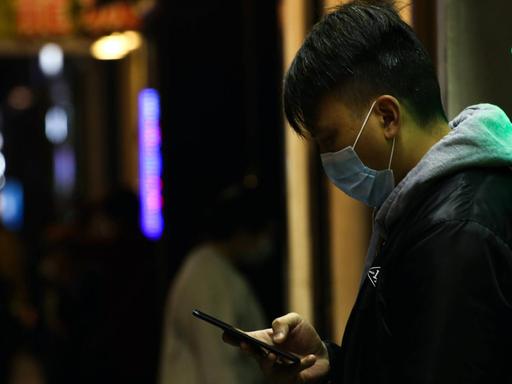 Ein Mann trägt eine Gesichtsmaske und blickt auf sein Smartphone.