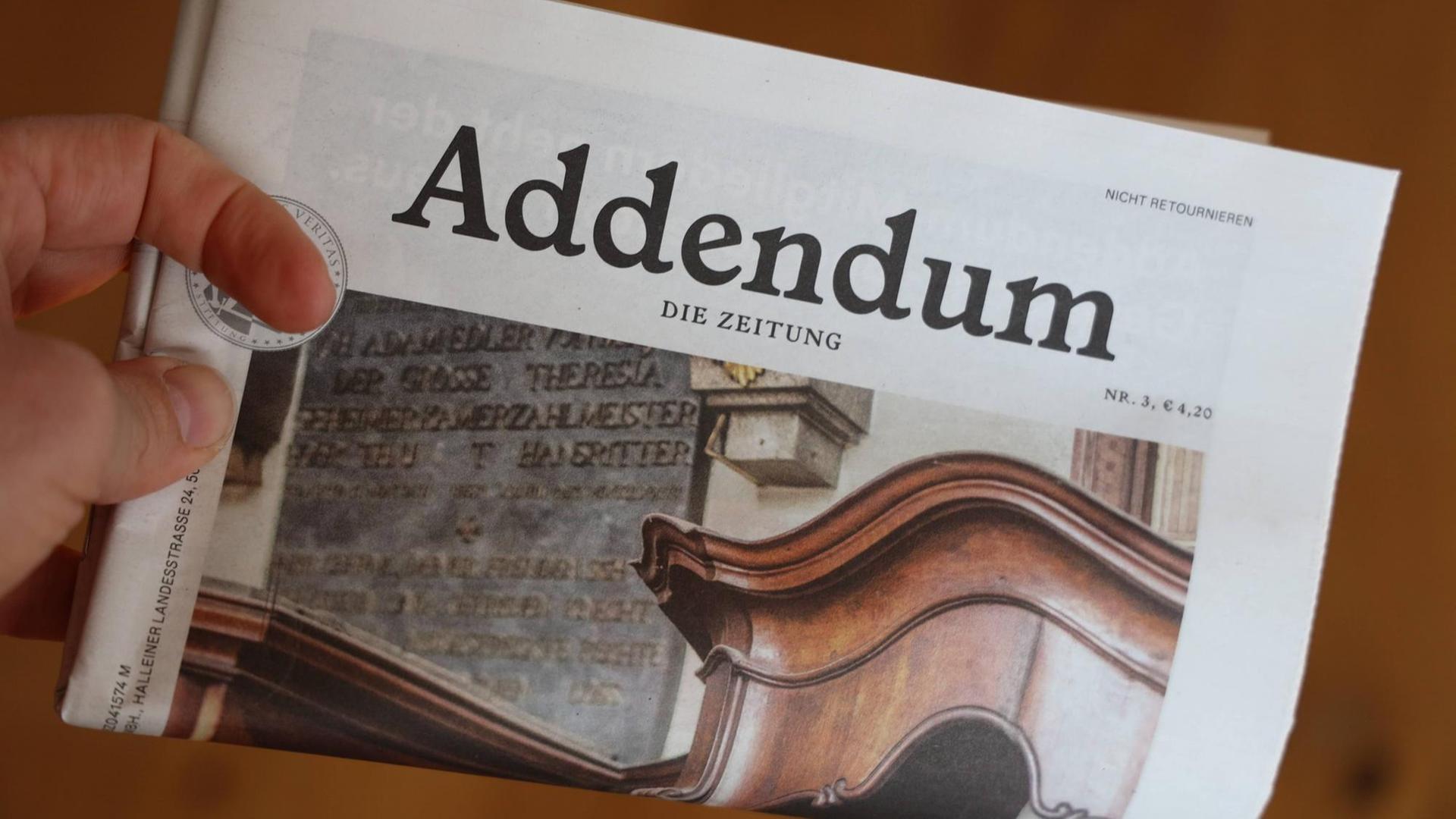 Eine Hand hält eine in der Mitte geknickte Ausgabe der Zeitschrift "Addendum".