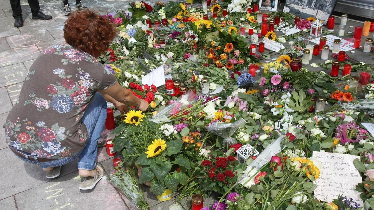 Eine Frau legt in Hamburg-Barmbek vor dem Supermarkt, in dem ein Mann einen Menschen mit einem Messer getötet hat, Blumen nieder. Eine Frau legt in Hamburg-Barmbek vor dem Supermarkt, in dem ein Mann einen Menschen mit einem Messer getötet hat, Blumen nieder.