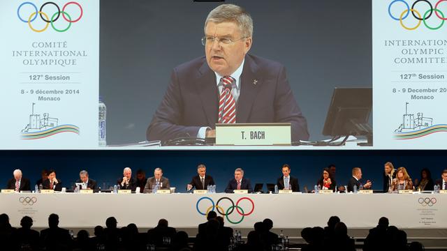IOC-Präsident Bach spricht vor den Mitgliedern beim IOC-Reformgipfel in Monaco. Über ihm ist er noch einmal auf einem übergroßen Bildschirm zu sehen.
