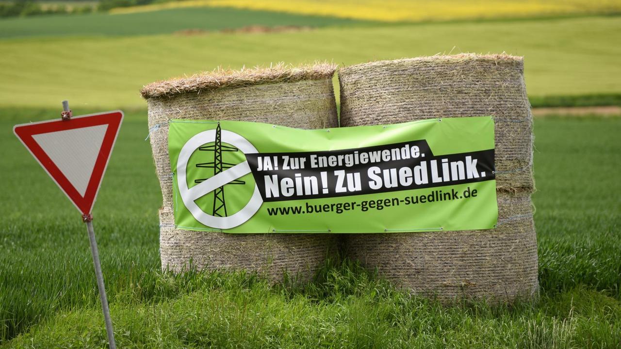Auf Heuballen prangt am 20.05.2015 an einer Straße bei Fritzlar (Hessen) ein Transparent der Gegner der Stromtrasse Suedlink. Zuletzt gab es Ablehnung und Kritik über den Vorstoß der bayerischen CSU, die Stromtrasse SuedLink zu Lasten Baden-Württembergs und Hessens nach Westen zu verlegen. Foto: Uwe Zucchi /dpa Auf Heuballen prangt am 20.05.2015 an einer Straße bei Fritzlar (Hessen) ein Transparent der Gegner der Stromtrasse Suedlink. Zuletzt gab es Ablehnung und Kritik über den Vorstoß der bayerischen CSU, die Stromtrasse SuedLink zu Lasten Baden-Württembergs und Hessens nach Westen zu verlegen. Foto: Uwe Zucchi /dpa