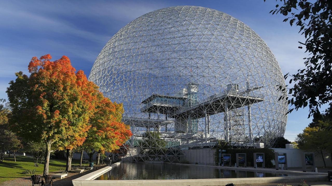 Das Äußere des Umweltmuseums Biosphère in Montreal. Eine transparente Kuppel in einem Parkgelände mit einem kleinen Teich im Vordergrund.