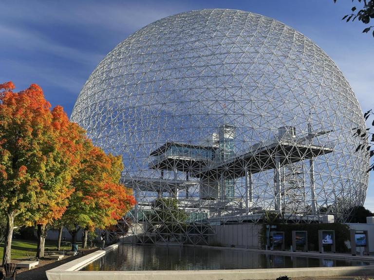 Das Äußere des Umweltmuseums Biosphère in Montreal. Eine transparente Kuppel in einem Parkgelände mit einem kleinen Teich im Vordergrund.