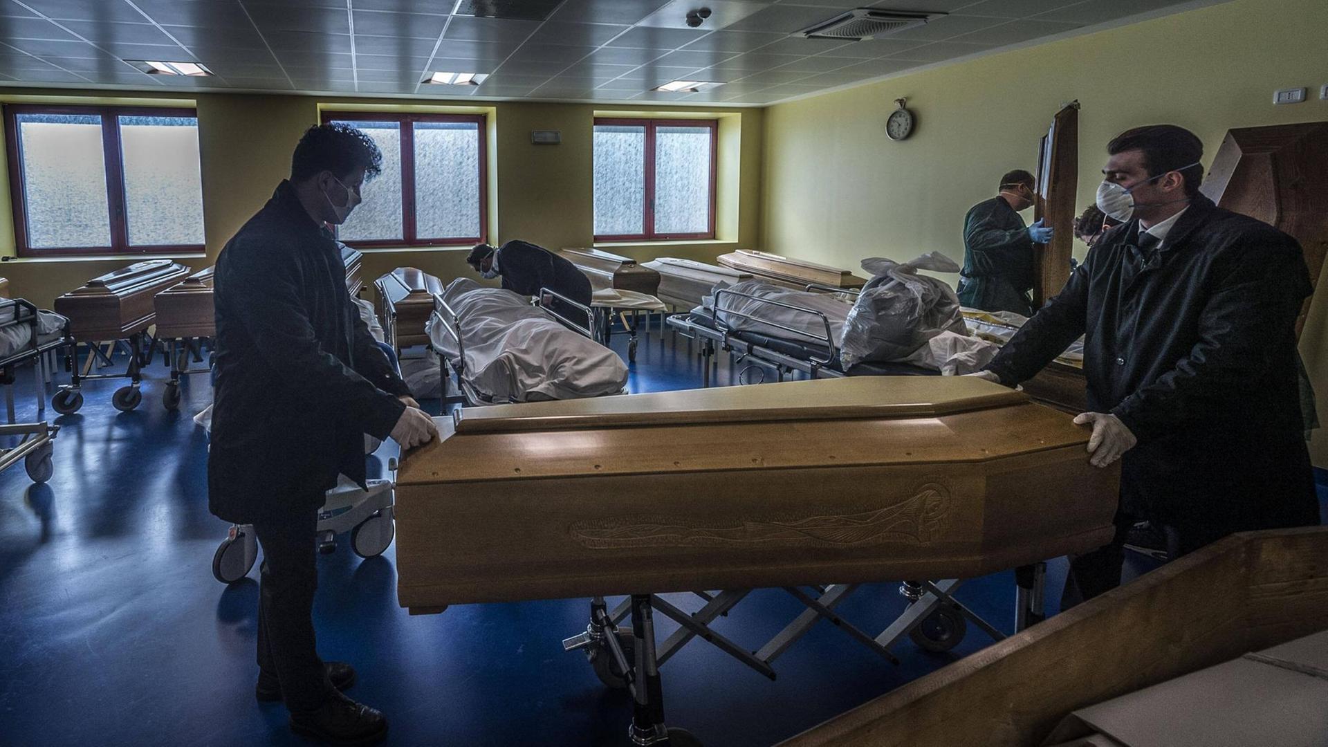 Träger mit Mundschutz und Handschuhen rollen einen Sarg aus einer Leichenhalle Träger mit Mundschutz und Handschuhen rollen einen Sarg aus einer Leichenhalle