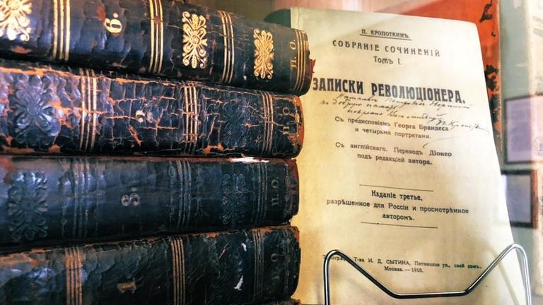 Mehrere dicke schwarze Bände, sichtbar alt, übereinander gestapelt, daneben ein Cover in Russisch. Mehrere dicke schwarze Bände, sichtbar alt, übereinander gestapelt, daneben ein Cover in Russisch.