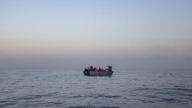 Bootsflüchtlinge aus Afrika und Asien winken auf einem Holzboot im Mittelmeer, 14 Meilen nördlich von Sabratha, Libyen, während sie auf ihre Rettung durch eine NGO warten