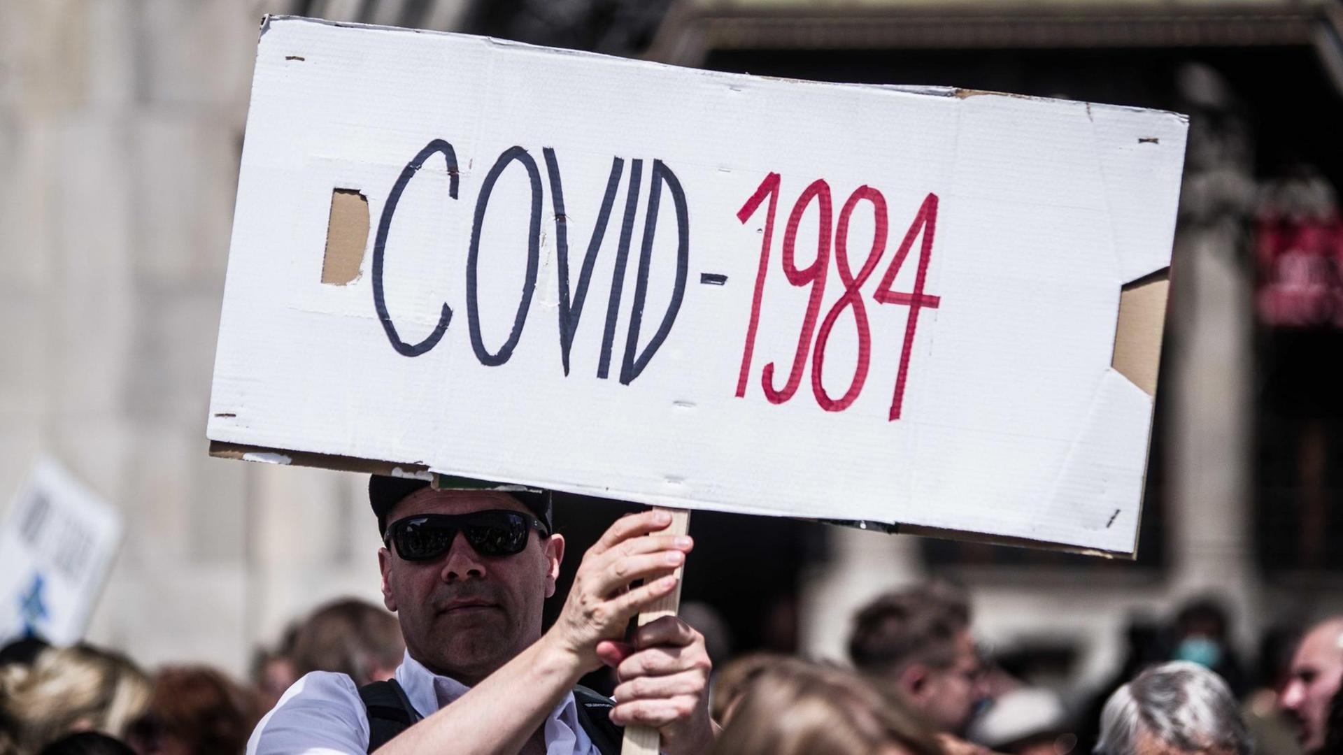 Ein Mann hält auf einer Hygienedemo in München ein Plakat mit der Aufschrift "COVID-1984" hoch Ein Mann hält auf einer Hygienedemo in München ein Plakat mit der Aufschrift "COVID-1984" hoch