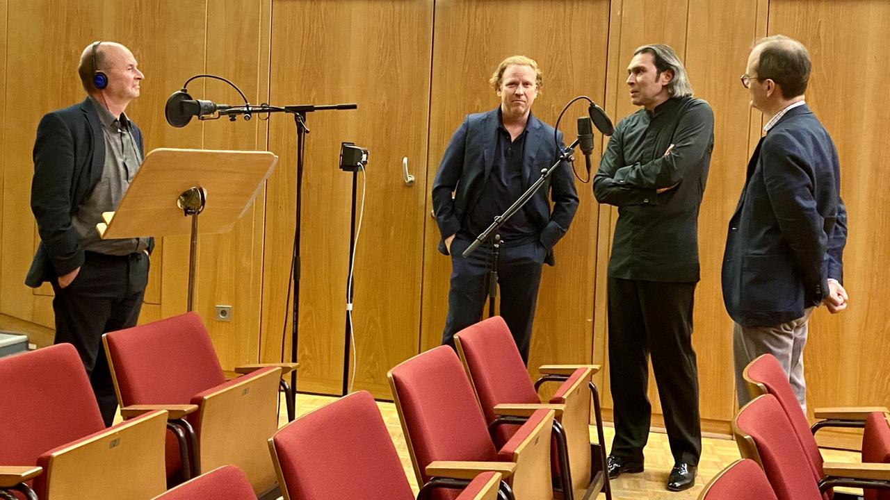 Vier Männer in einem Gespräch vor Mikrofonen vertieft.