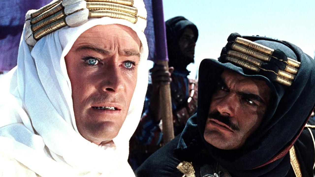 Peter O'Toole blickt bedeutungsschwanger ins Off des Bildes, während Omar Sharif ihn anspricht. Beide tragen Beduinenkleidung. Peter O'Toole blickt bedeutungsschwanger ins Off des Bildes, während Omar Sharif ihn anspricht. Beide tragen Beduinenkleidung.