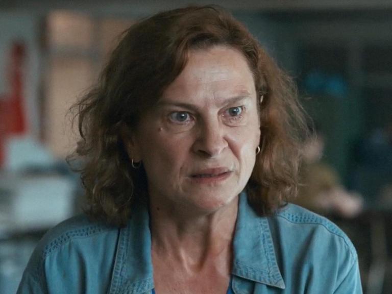 Eine Frau trägt eine türkise Bluse und blickt ärgerlich.