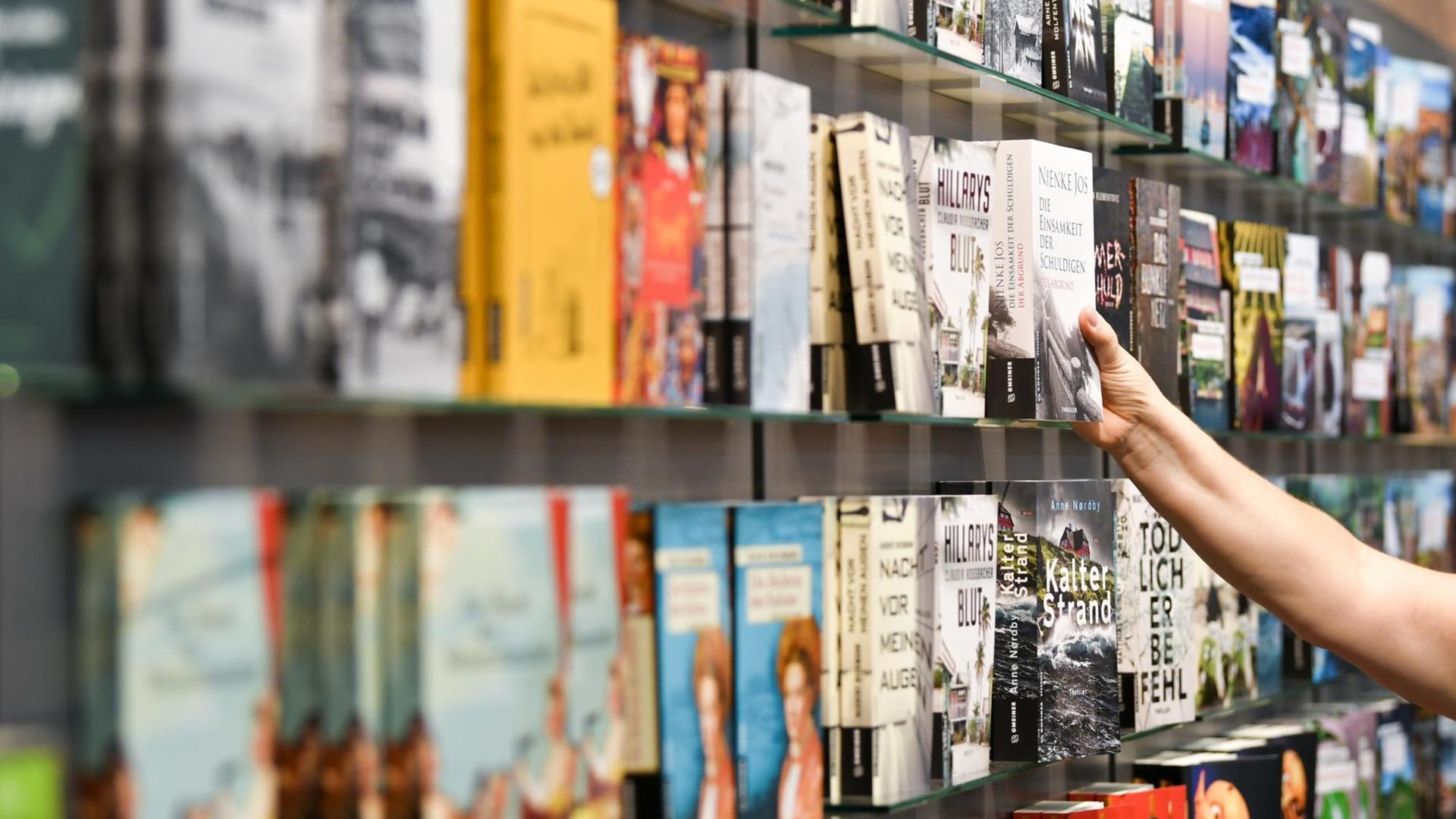Eine Hand greift nach einem Buch in einem Bücherregal. Eine Hand greift nach einem Buch in einem Bücherregal.