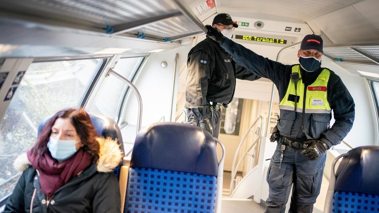 07.12.2020, Berlin: Beamte der Bundespolizei und der DB-Sicherheit stehen in einem Regionalzug vom Berliner Hauptbahnhof zum Flughafen BER neben einem Fahrgast. 