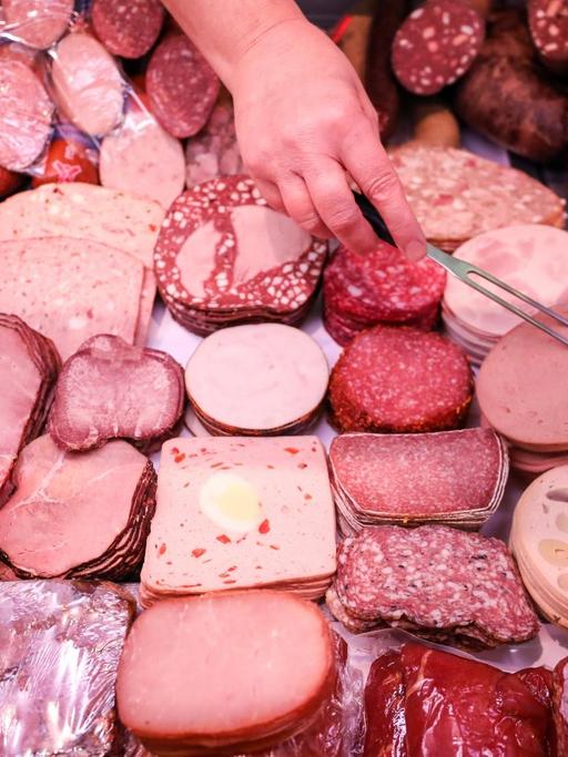 Eine Verkäuferin nimmt Leberkäse aus einer Fleischtheke in einem Supermarkt.