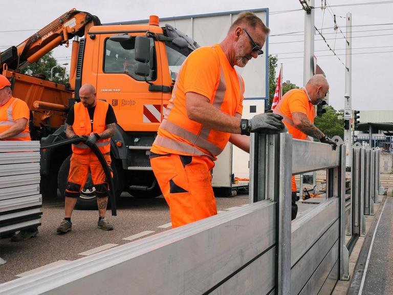 Mitarbeiter der Stadt Dresden bauen an einer Straße eine mobile Hochwasserschutzanlage zur Probe auf.