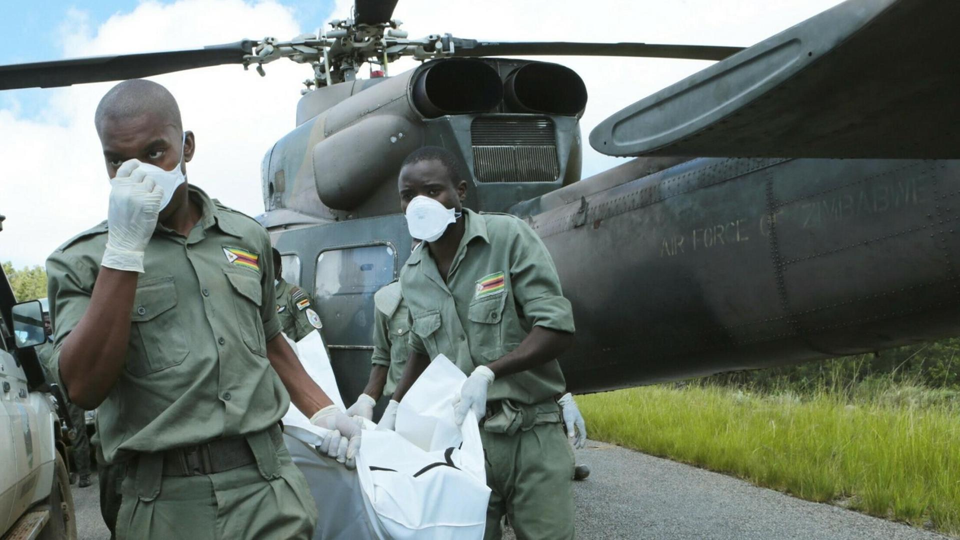Rettungskräfte sind vor einem Hubschrauber zu sehen, die tragen einen großen weißen Sack. Rettungskräfte sind vor einem Hubschrauber zu sehen, die tragen einen großen weißen Sack.