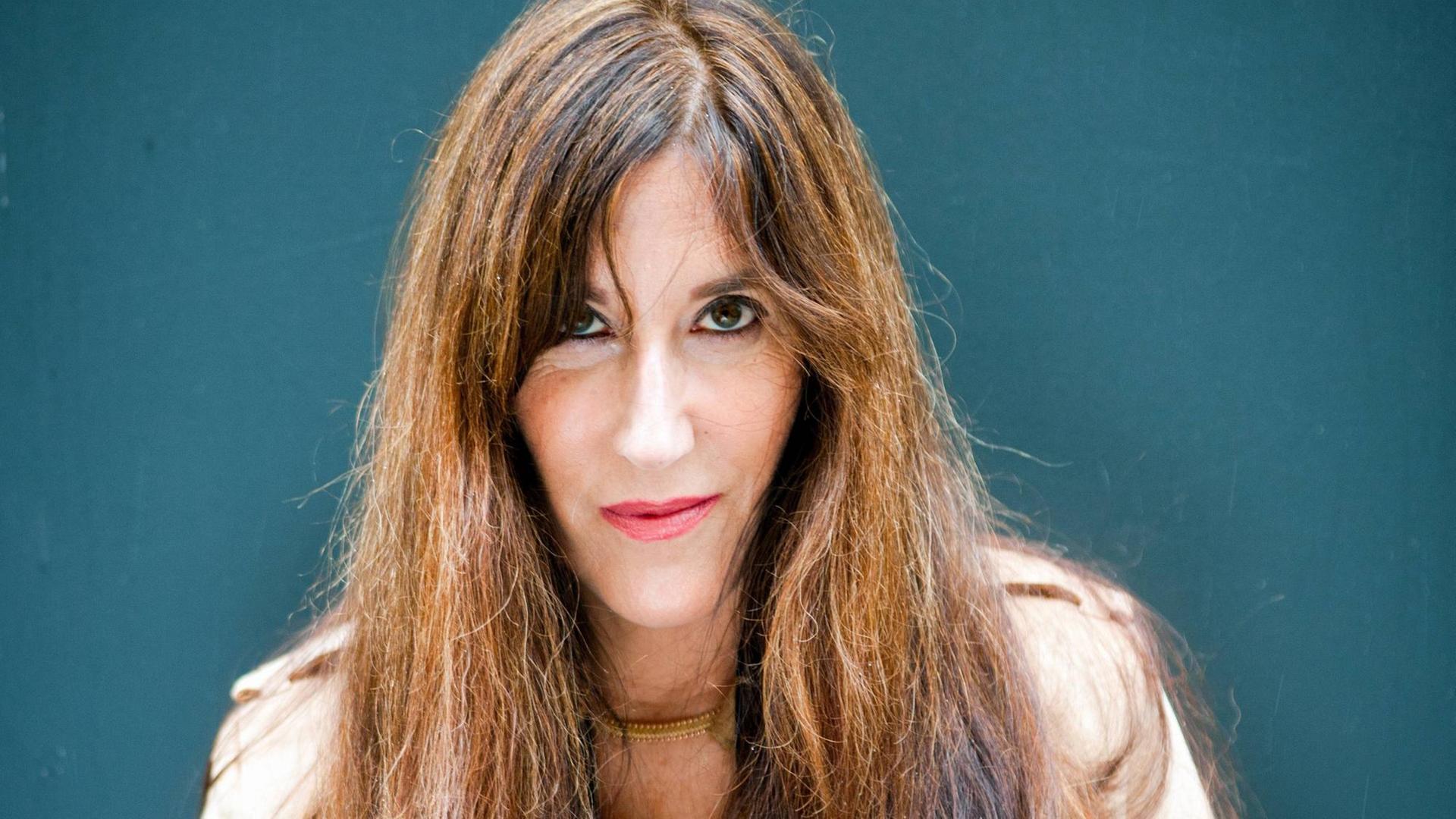 Zeruya Shalev mit langen braunen Haaren schaut vor türkisem Hintergrund entschlossen in die Kamera. Zeruya Shalev mit langen braunen Haaren schaut vor türkisem Hintergrund entschlossen in die Kamera.