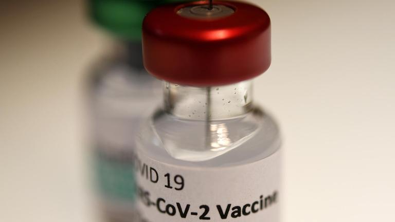 Eine Spritze steckt in einem Fläschchen mit dem Aufdruck "COVID-19 Vaccine"