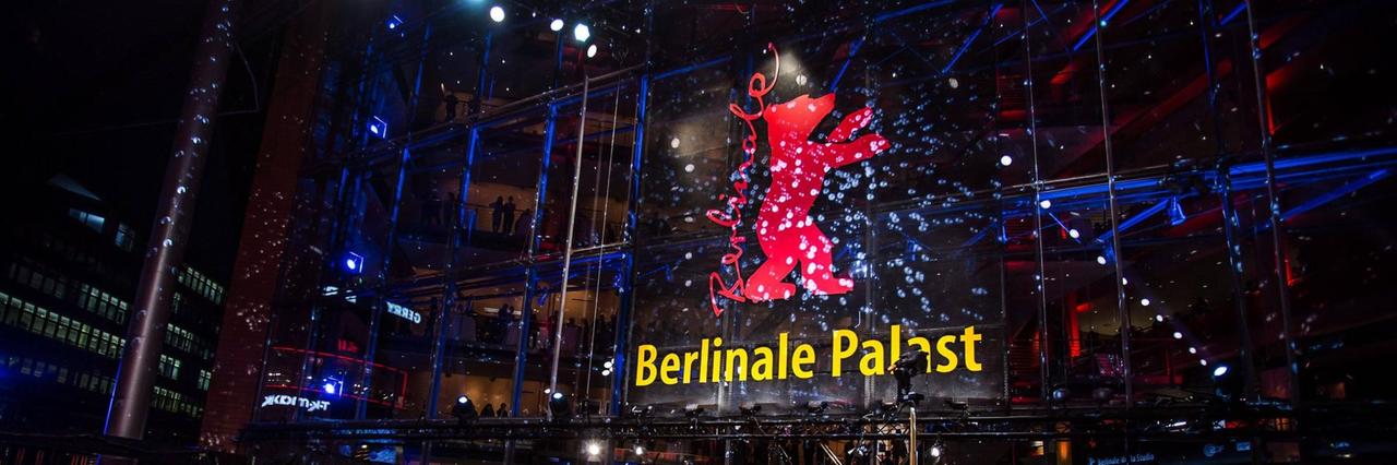 Der Berlinale-Palast am Abend, mit dem roten Bären an der Glasfront, davor viele Menschen auf und neben dem roten Teppich  