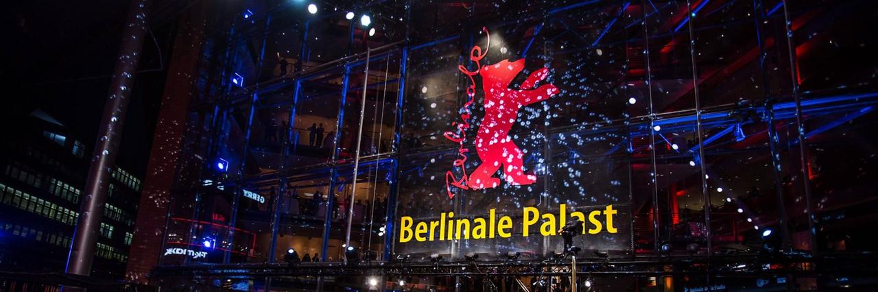 Der Berlinale-Palast am Abend, mit dem roten Bären an der Glasfront, davor viele Menschen auf und neben dem roten Teppich Der Berlinale-Palast am Abend, mit dem roten Bären an der Glasfront, davor viele Menschen auf und neben dem roten Teppich