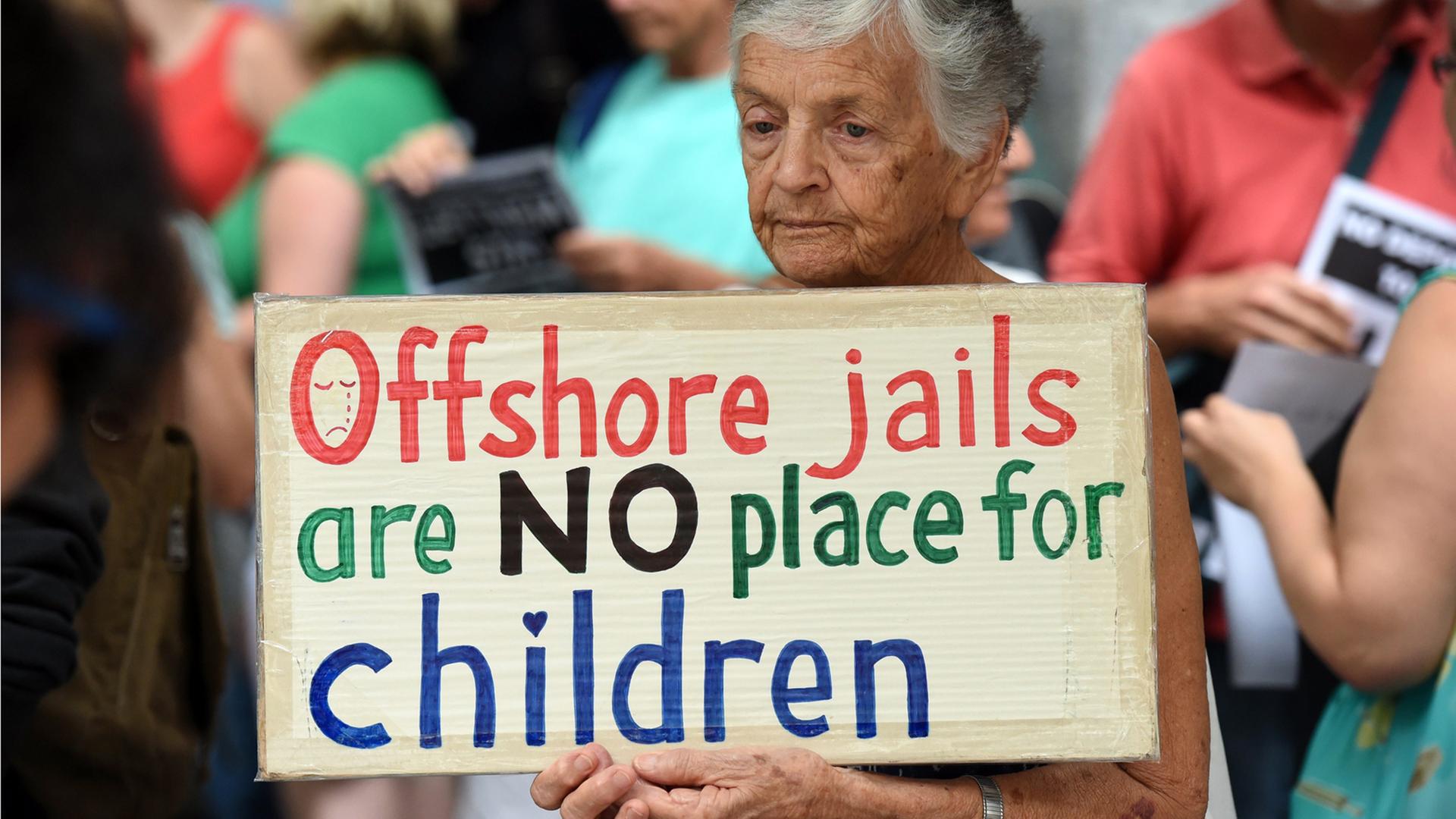 Eine ältere Frau demonstriert gegen die Unterbringung von Flüchtlingskindern auf der australischen Insel Nauru. "Offshore Jails are NO place for children", steht auf ihrem Plakat. Eine ältere Frau demonstriert gegen die Unterbringung von Flüchtlingskindern auf der australischen Insel Nauru. "Offshore Jails are NO place for children", steht auf ihrem Plakat.