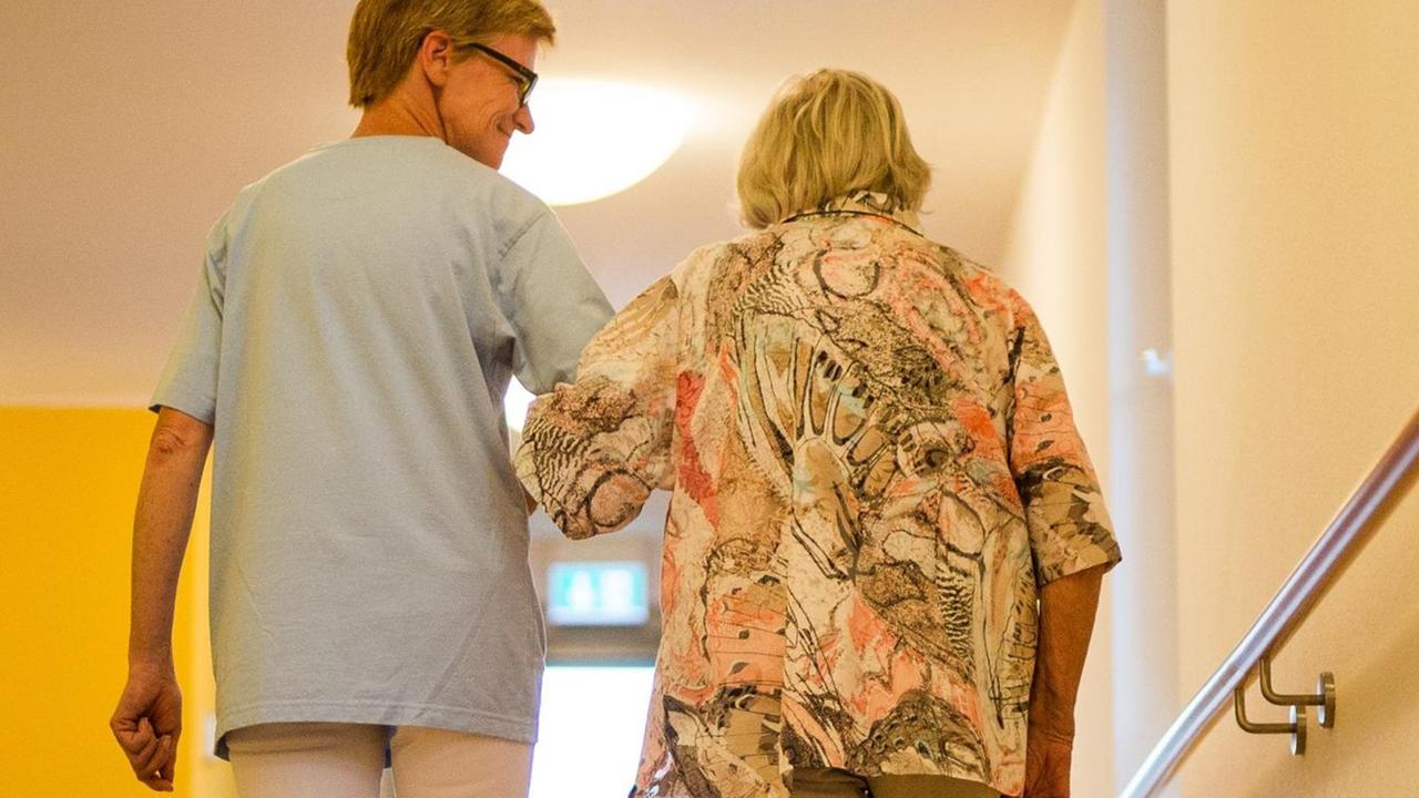 Eine Pflegekraft geht in einem Pflegeheim mit einer älteren Dame über einen Korridor. Eine Pflegekraft geht in einem Pflegeheim mit einer älteren Dame über einen Korridor.