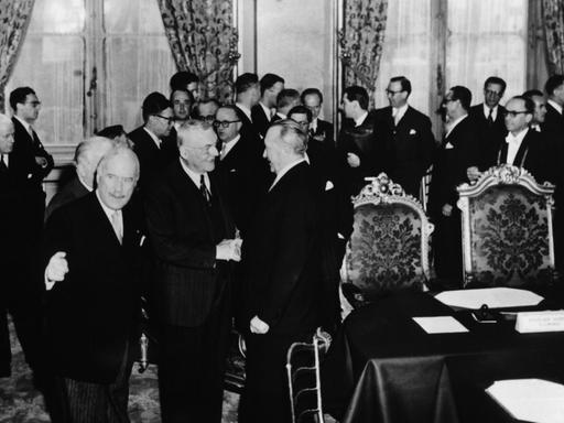 Ein Blick in den Unterzeichnungssaal am Quai d'Orsay in Paris am 23.10.1954 zeigt US-Außenminister John Foster Dulles (M), der gerade Bundeskanzler Konrad Adenauer (rechts von Dulles) begrüßt, kurz vor der Unterzeichnung der Pariser Verträge. Links von Dulles der französische Hohe Kommissar André Francois-Poncet (l, Richtung Kamera blickend).