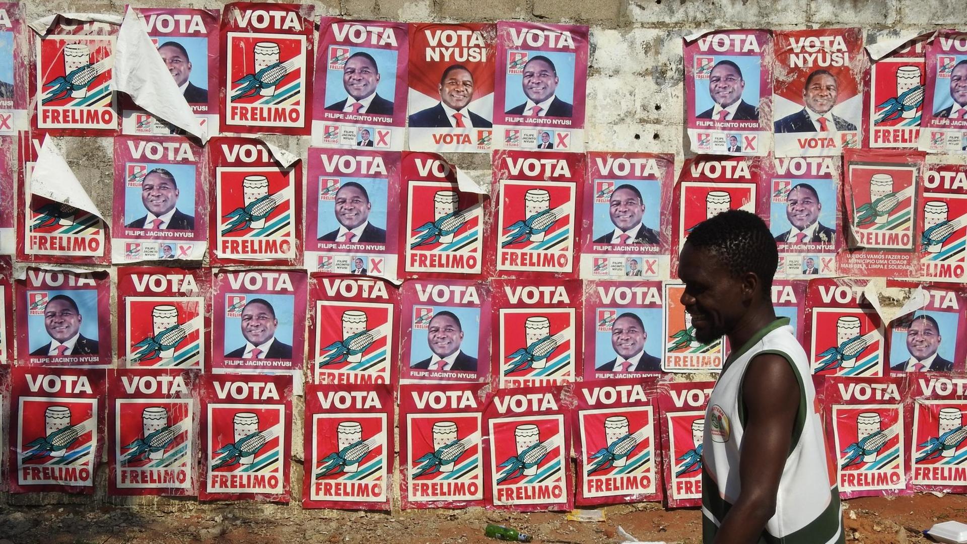 Ein Mann läuft in Maputo an einer Wand entlang, die mit roten Plakaten des mosambikanischen Staatschefs Filipe Jacinto Nyusi von der Frelimo beklebt ist. Ein Mann läuft in Maputo an einer Wand entlang, die mit roten Plakaten des mosambikanischen Staatschefs Filipe Jacinto Nyusi von der Frelimo beklebt ist.
