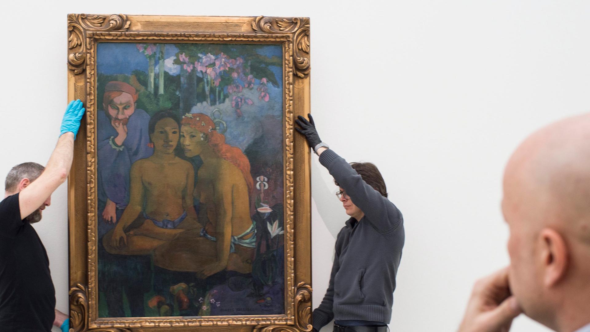 Zwei Mitarbeiter hängen das Gemälde auf, das Sam Keller mit der Hand am Kinn betrachtet.