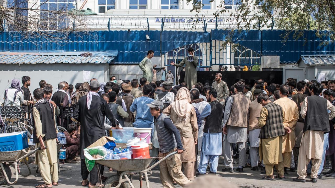 Eine Menschentraube steht wartend vor einer Bank und hofft darauf, ein wenig Cash zu erhalten. Ein Mann mit einem Megafon ruft einzelne Menschen auf, die berechtigt sind, Geld zu erhalten. Seit dem die Taliban an der Macht sind, ist die Wirtschaft kollabiert und es herrscht ein massive Engpässe an Bargeld. Eine Menschentraube steht wartend vor einer Bank und hofft darauf, ein wenig Cash zu erhalten. Ein Mann mit einem Megafon ruft einzelne Menschen auf, die berechtigt sind, Geld zu erhalten. Seit dem die Taliban an der Macht sind, ist die Wirtschaft kollabiert und es herrscht ein massive Engpässe an Bargeld.