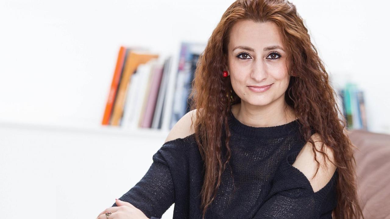 Widad Nabi sitzt bei einer Lesung auf einem Sofa und schaut in die Kamera. Widad Nabi sitzt bei einer Lesung auf einem Sofa und schaut in die Kamera.