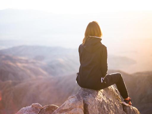 Eine Frau sitzt auf dem Gipfel eines Berges, den Rücken zur Kamera.