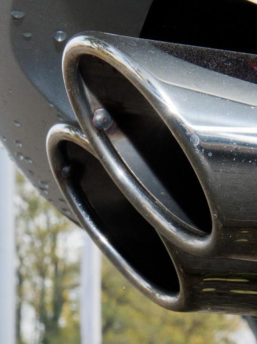 Ein Auspuff eines Autos mit einem VW-Logo im Hintergrund.