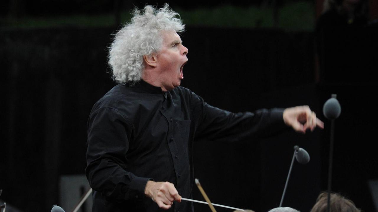 Dirigent Sir Simon Rattle bei einem Klassikkonzert in der Waldbühne, wobei sein Körper im Einsatz ist. Er dirigiert mit erhobenem Taktstock, geöffnetem Mund und Einsatz gebender linker Hand Dirigent Sir Simon Rattle bei einem Klassikkonzert in der Waldbühne, wobei sein Körper im Einsatz ist. Er dirigiert mit erhobenem Taktstock, geöffnetem Mund und Einsatz gebender linker Hand