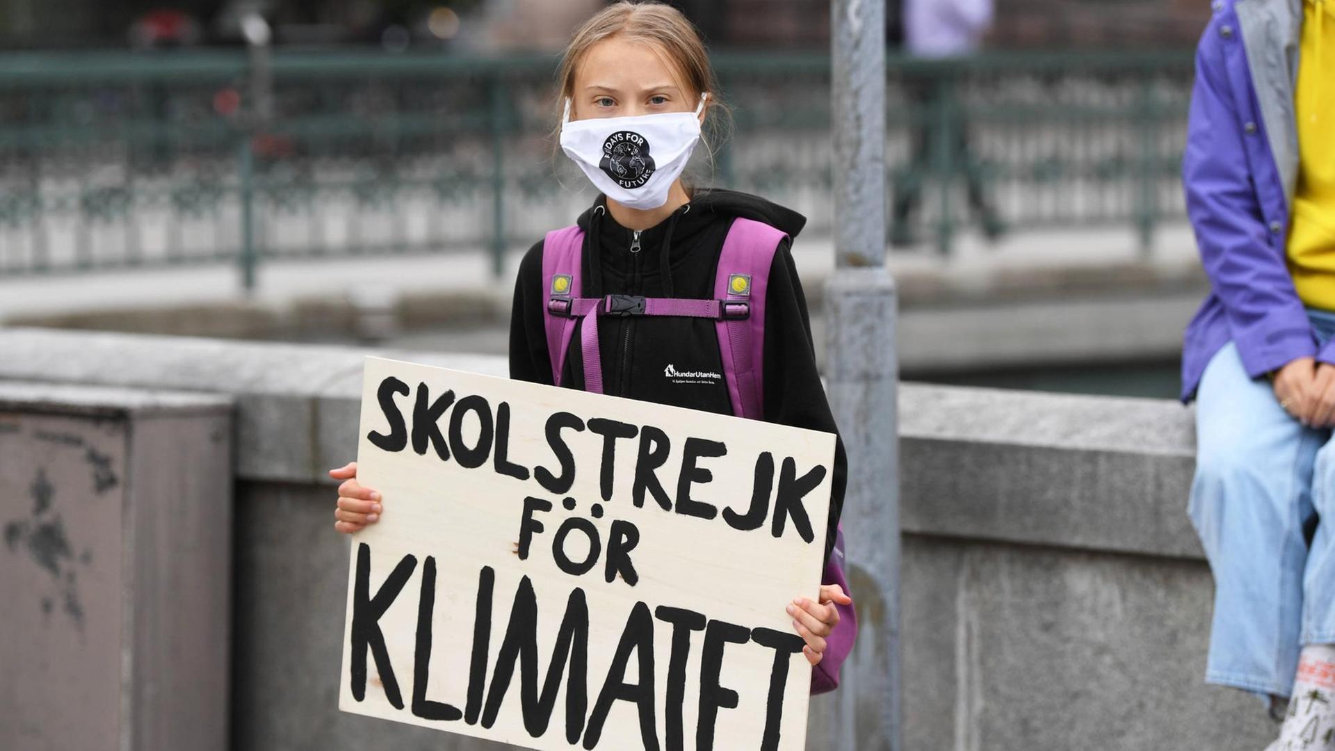 Greta Thunberg steht mit Maske und Schild (auf Deutsch: "Schulstreik für das Klima") vor dem schwedischen Parlament. Greta Thunberg steht mit Maske und Schild (auf Deutsch: "Schulstreik für das Klima") vor dem schwedischen Parlament.