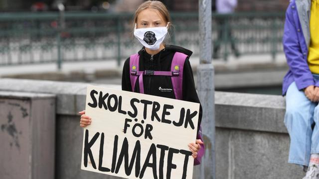 Greta Thunberg steht mit Maske und Schild (auf Deutsch: "Schulstreik für das Klima") vor dem schwedischen Parlament.